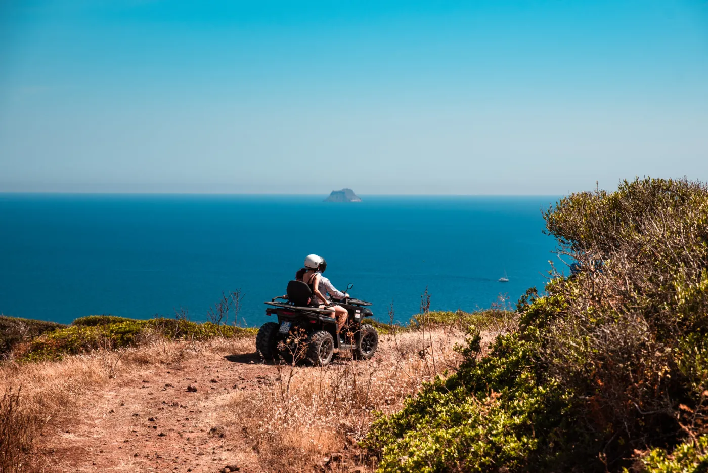 A quad with driver and passenger on a headland above the sea, Sant'Antioco